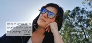 Autorretrato mirando al cielo con gafas y capucha negra, detrás unos eucaliptos altos con caja de texto: confía en la Vida, dale la oportunidad a que te muestre TODO, por AsunAdá