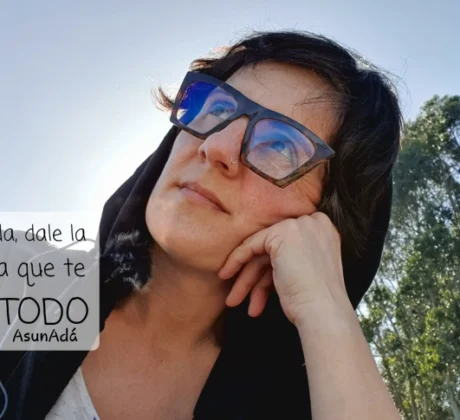 Autorretrato Asun Adá, mirando al cielo con gafas y capucha negra, detrás unos eucaliptos altos con caja de texto: confía en la Vida, dale la oportunidad a que te muestre TODO, por AsunAdá